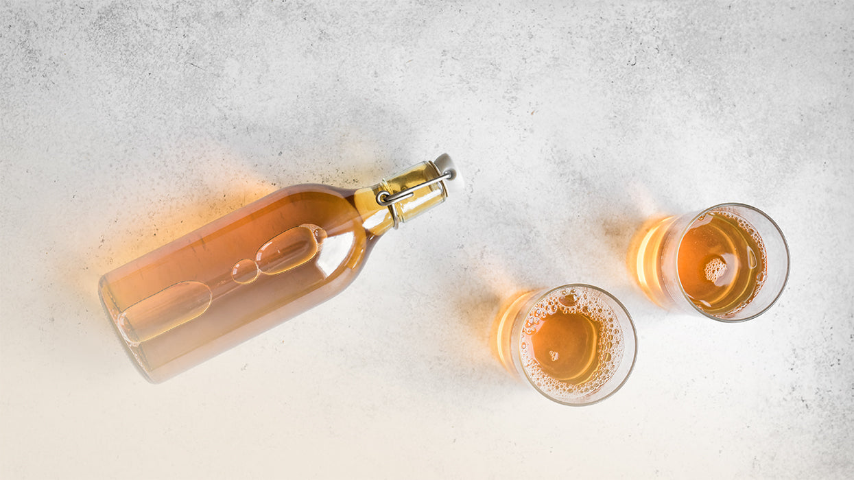 Liegende Glasflasche zwei Glaeser mit Kombucha