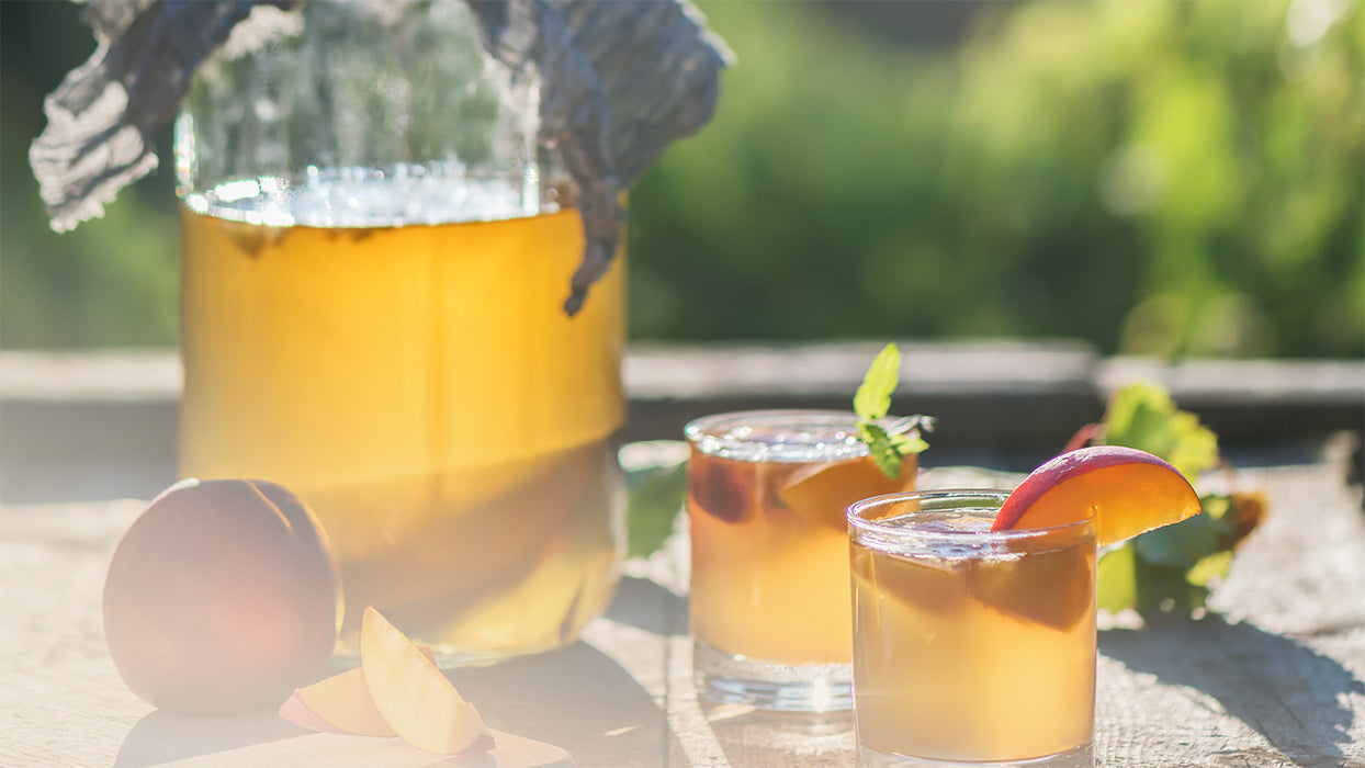 Kombucha Pfirsich Eistee Glasbehaelter zwei Glaeser Pfirsiche draussen Abendsonne